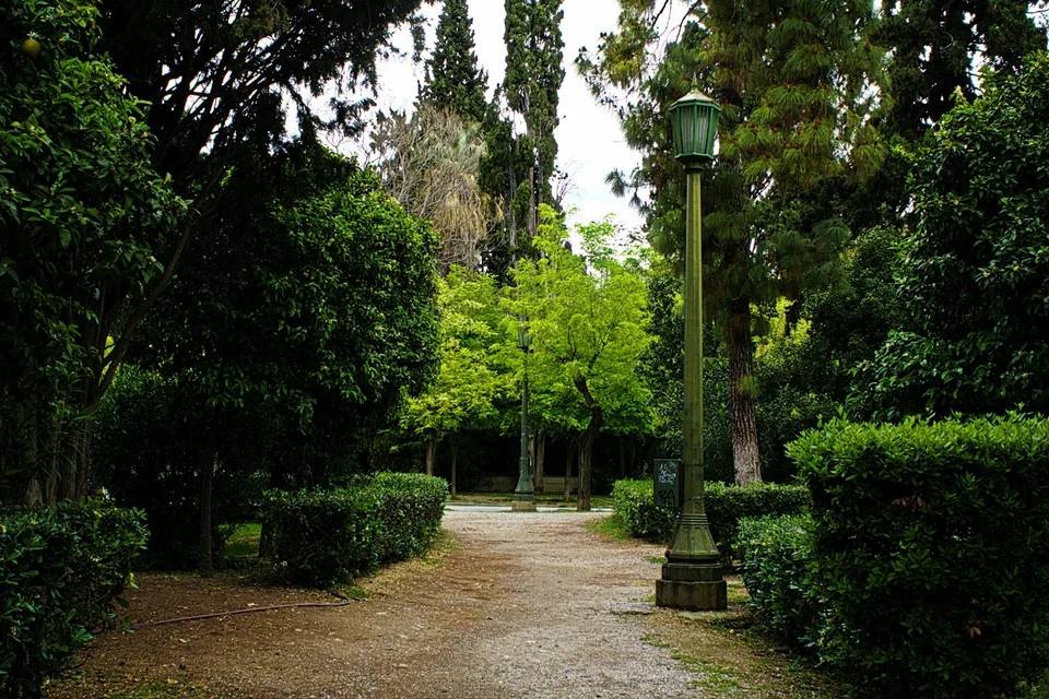 Χωμάτινο μονοπάτι με δέντρα και θάμνους σε πάρκο της Αθήνας, με παλιού τύπου φανοστάτη